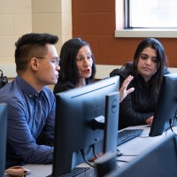 two students listening to instructor in front of a computer