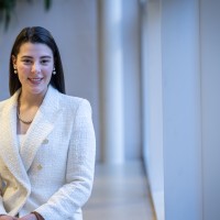 A female accounting student smiling and posing while sitting on a bench in a bright hallway at the Fanshawe College campus