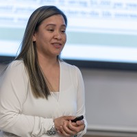 A female Asian student is standing to present financial statements in a classroom