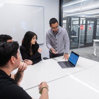 man standing points to laptop on table while three people watch