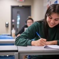 person smiling while writing in notebook