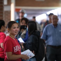 Two volunteers in red shirts stand in the hall during orientation helping people with directions, hanging out maps
