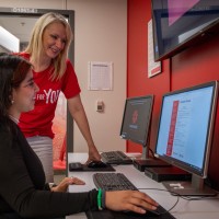 advisor stands next to student who is editing resume on computer