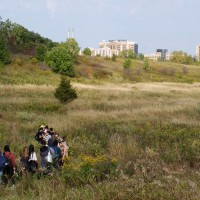 Honours Bachelor of Environmental Design and Planning students stand in grassy field in front of city skyline