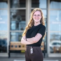 A Fanshawe grad posing in front of a building entrance with their hands crossed and smiling