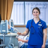 Photo of a nursing student in blue scrubs wearing a stethoscope posing for the camera while wearing at