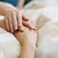 A comforting hand rests gently on another's, conveying empathy and support. The hands lie on a patterned beige blanket, suggesting a serene atmosphere.