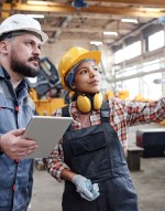 woman in hardhat points and talks as man listens