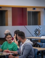 Two people sit at a table, one in a green shirt and the other in a grey hoodie, engaged in conversation.