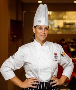 Chef Erin Circelli-Russell stands in the Chef's Table dinning room in chef coat and hat