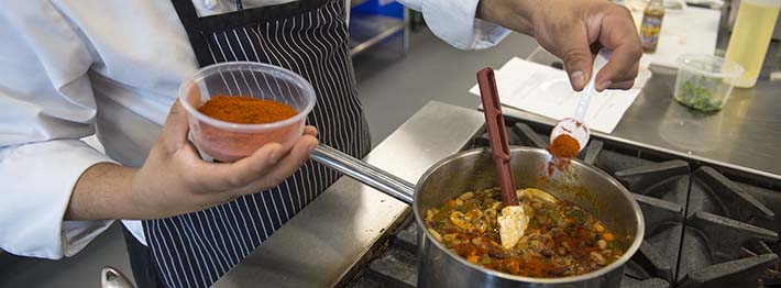 Chef adding spices to chili